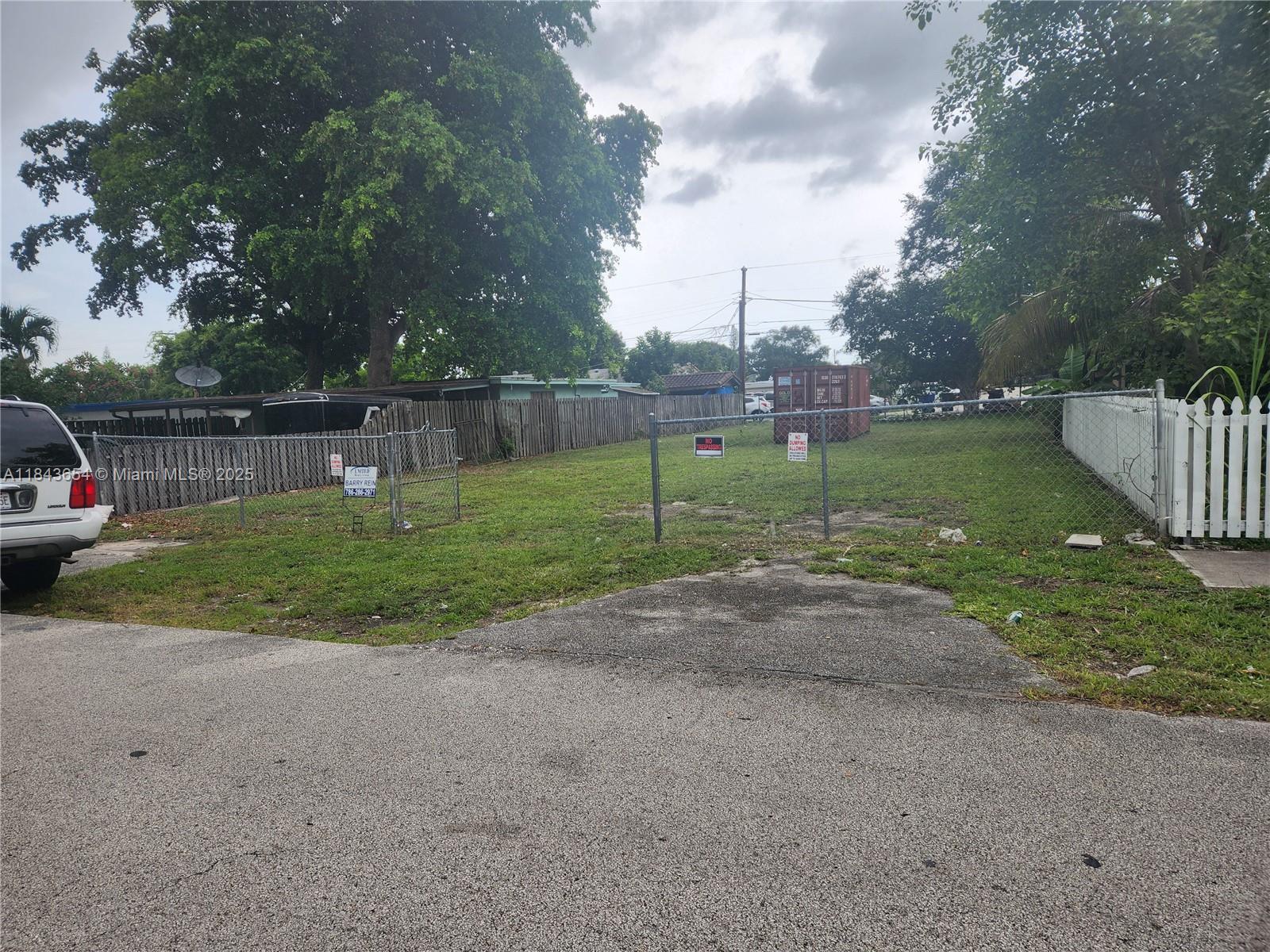 A fenced, grassy vacant lot sits between residential properties under a cloudy sky — 315 N 61st Ave, Hollywood FL 33024, HOLLYWOOD, FL