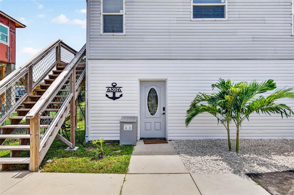 An exterior view of a house with white siding, an outdoor staircase, and an anchor sign — 6806 SEA RANCH DRIVE, HUDSON, FL
