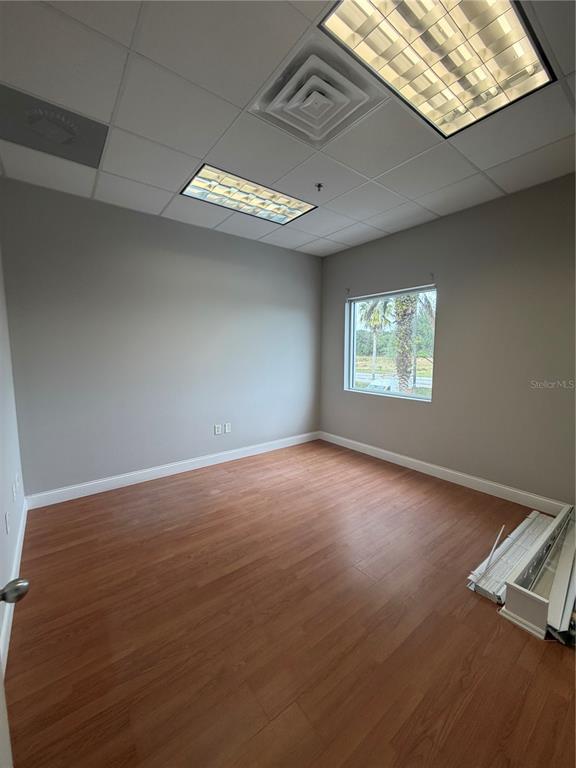 An empty office with wood-look flooring, a drop ceiling, and a window overlooking trees — 245 BELLAGIO CIRCLE, SANFORD, FL