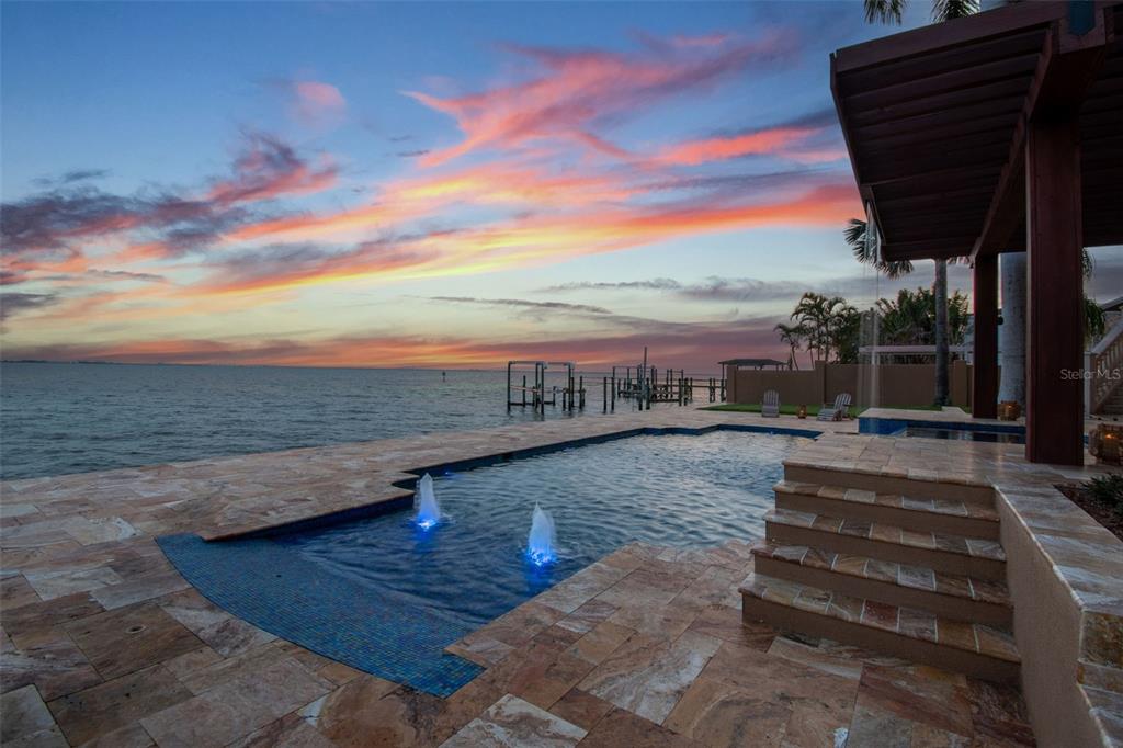 A swimming pool with fountains overlooks a bay at sunset from a stone patio — 5810 MARINER STREET, TAMPA, FL