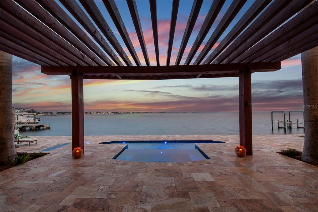 A stone patio features a rectangular pool under a wooden pergola overlooking the open water — 5810 MARINER STREET, TAMPA, FL