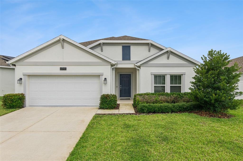 A single-story house with a white stucco exterior, a two-car garage, and a front lawn — 6941 DILLY LAKE AVENUE, GROVELAND, FL