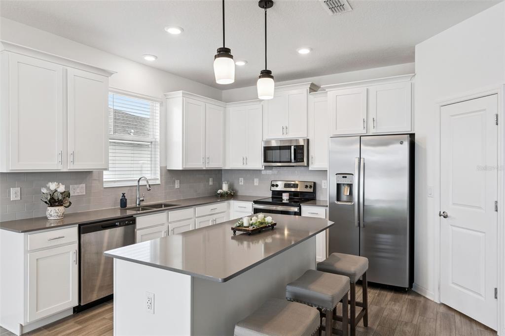 A modern kitchen features white cabinetry, gray countertops, a center island, and stainless steel appliances — 6941 DILLY LAKE AVENUE, GROVELAND, FL