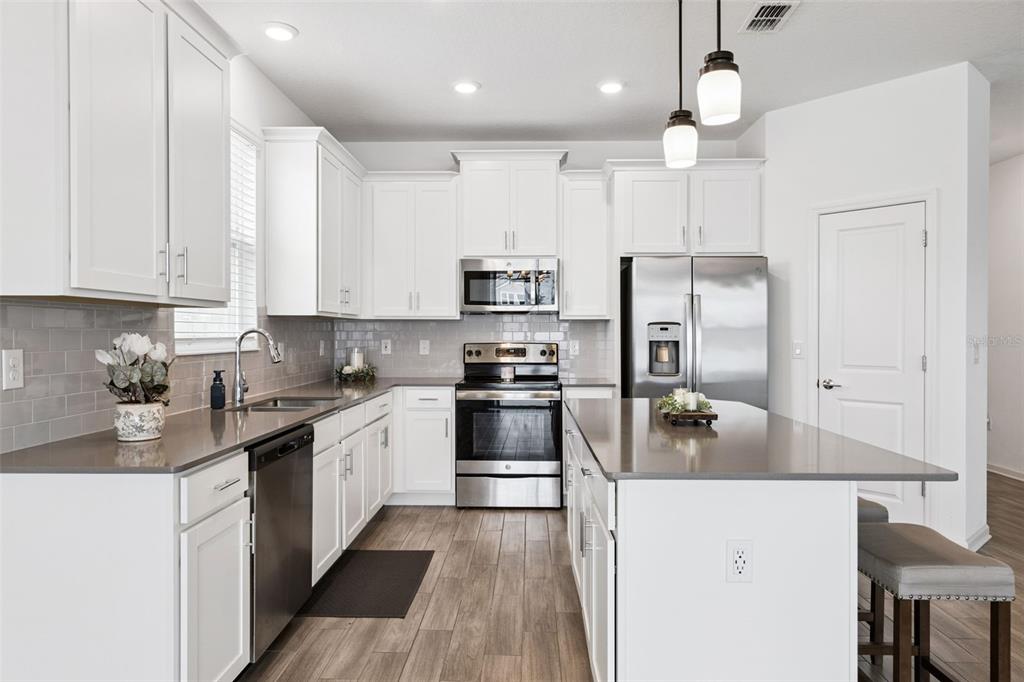 A modern kitchen features white cabinets, stainless steel appliances, gray countertops, and wood-look tile flooring — 6941 DILLY LAKE AVENUE, GROVELAND, FL