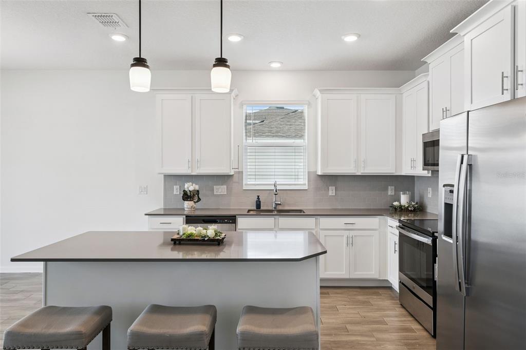 A kitchen features white cabinets, gray countertops, stainless steel appliances, and a central island — 6941 DILLY LAKE AVENUE, GROVELAND, FL