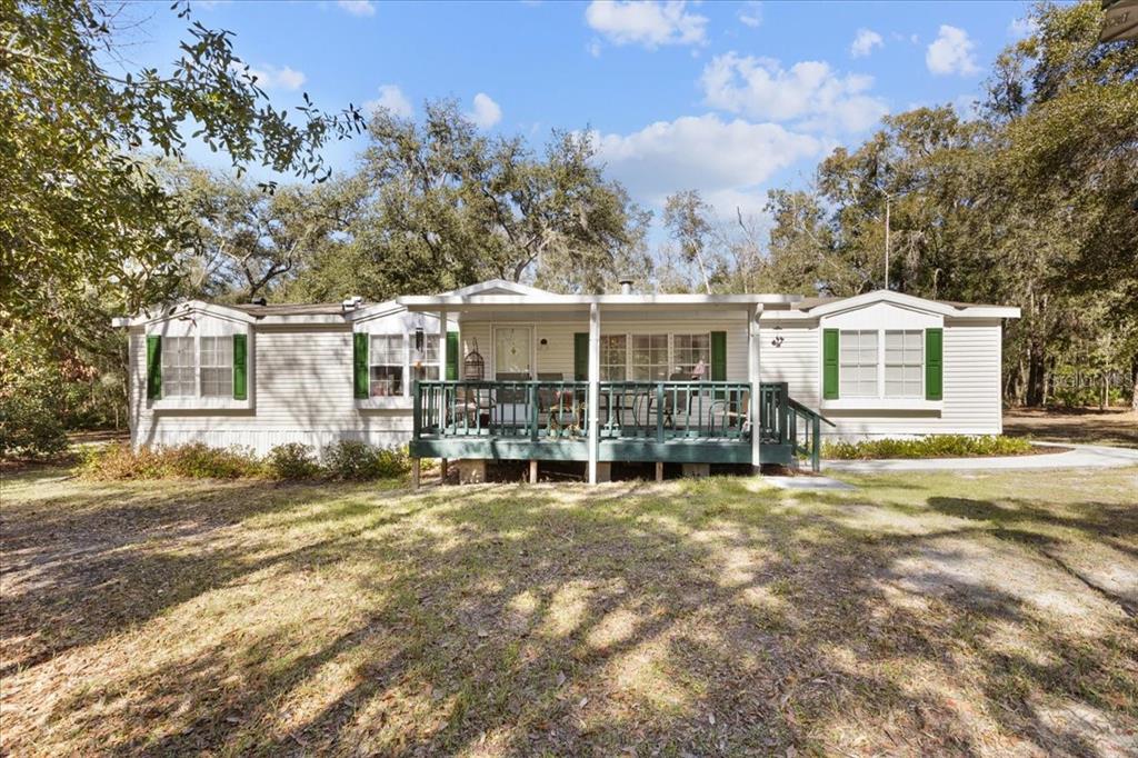 A single-story manufactured home with a front deck and green shutters sits in a wooded yard — 1658 NE 743RD STREET, OLD TOWN, FL