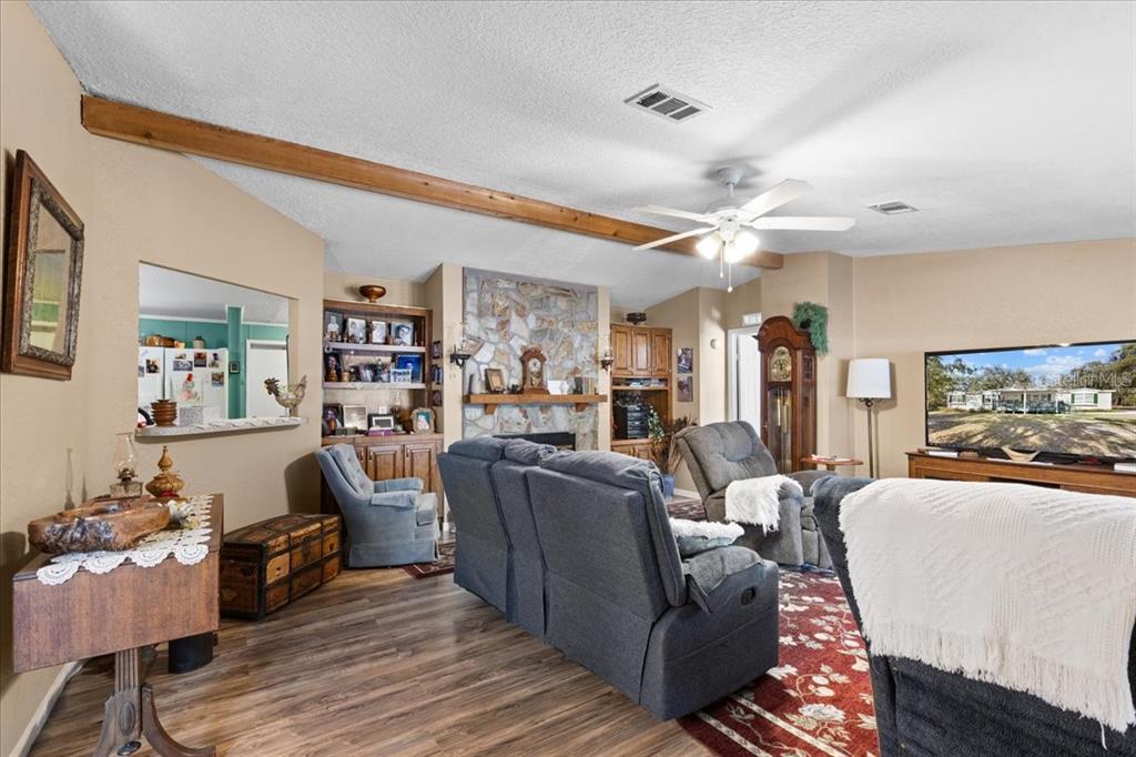 A living room features a stone fireplace, wood-look flooring, exposed ceiling beams, and gray furniture — 1658 NE 743RD STREET, OLD TOWN, FL