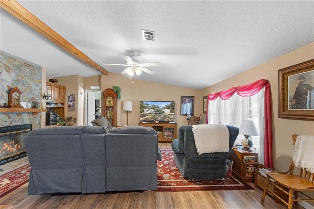 A living room features a stone fireplace, wood-look flooring, a ceiling fan, and a television — 1658 NE 743RD STREET, OLD TOWN, FL