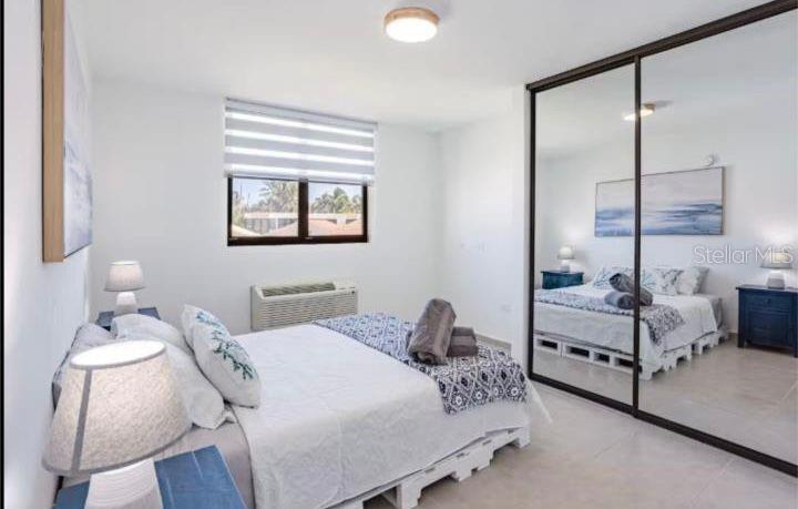 A bedroom features a bed with a pallet frame, mirrored closet doors, and a window — C-214 MARBELA CASA DE PLAYA, ISABELA, PR