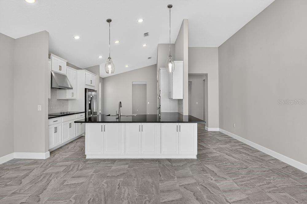 A modern kitchen features white cabinetry, black countertops, a central island, and gray tile flooring — 39 OCONEE DRIVE, PALM COAST, FL