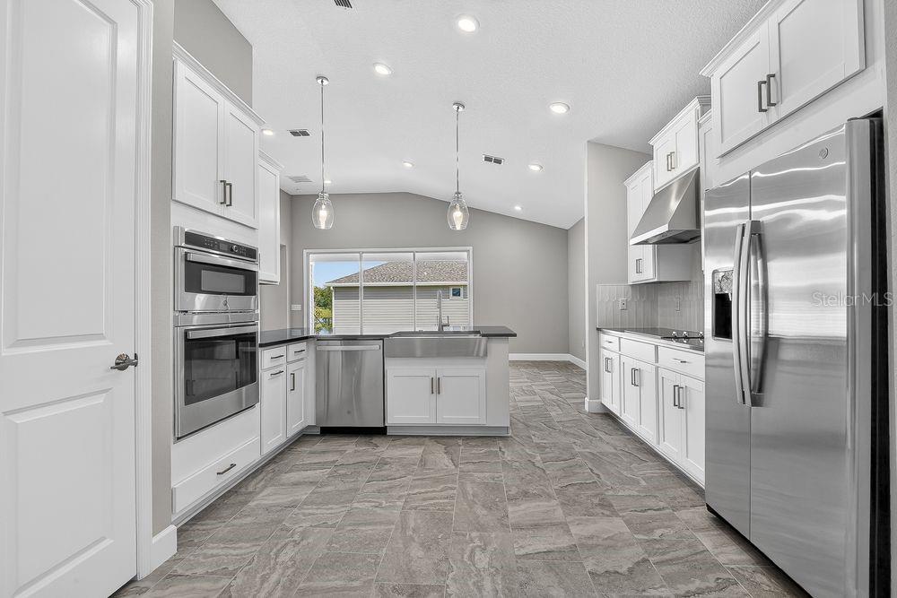A modern kitchen features white cabinetry, stainless steel appliances, a farmhouse sink, and tile flooring — 39 OCONEE DRIVE, PALM COAST, FL