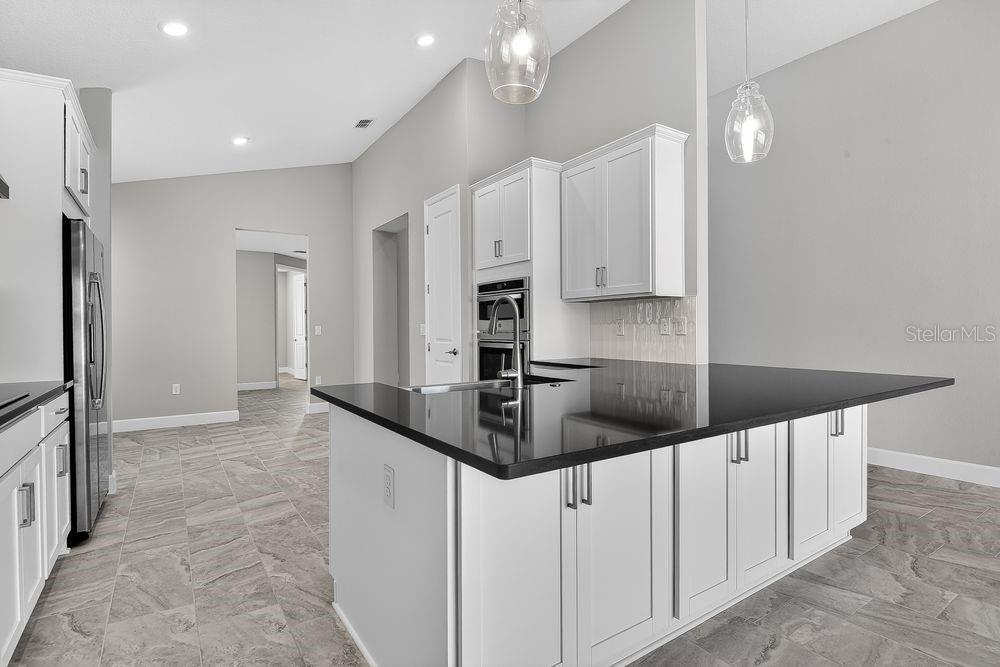 A kitchen features white cabinets, black countertops, a central island, and gray tile flooring — 39 OCONEE DRIVE, PALM COAST, FL