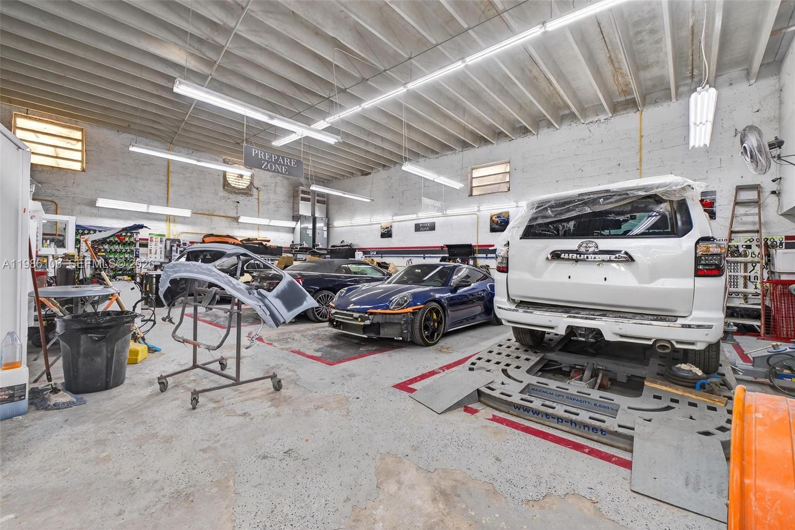 An auto body repair shop features a concrete floor, overhead lighting, and several vehicles undergoing service — 0000 NW 56, Doral FL 33166, DORAL, FL