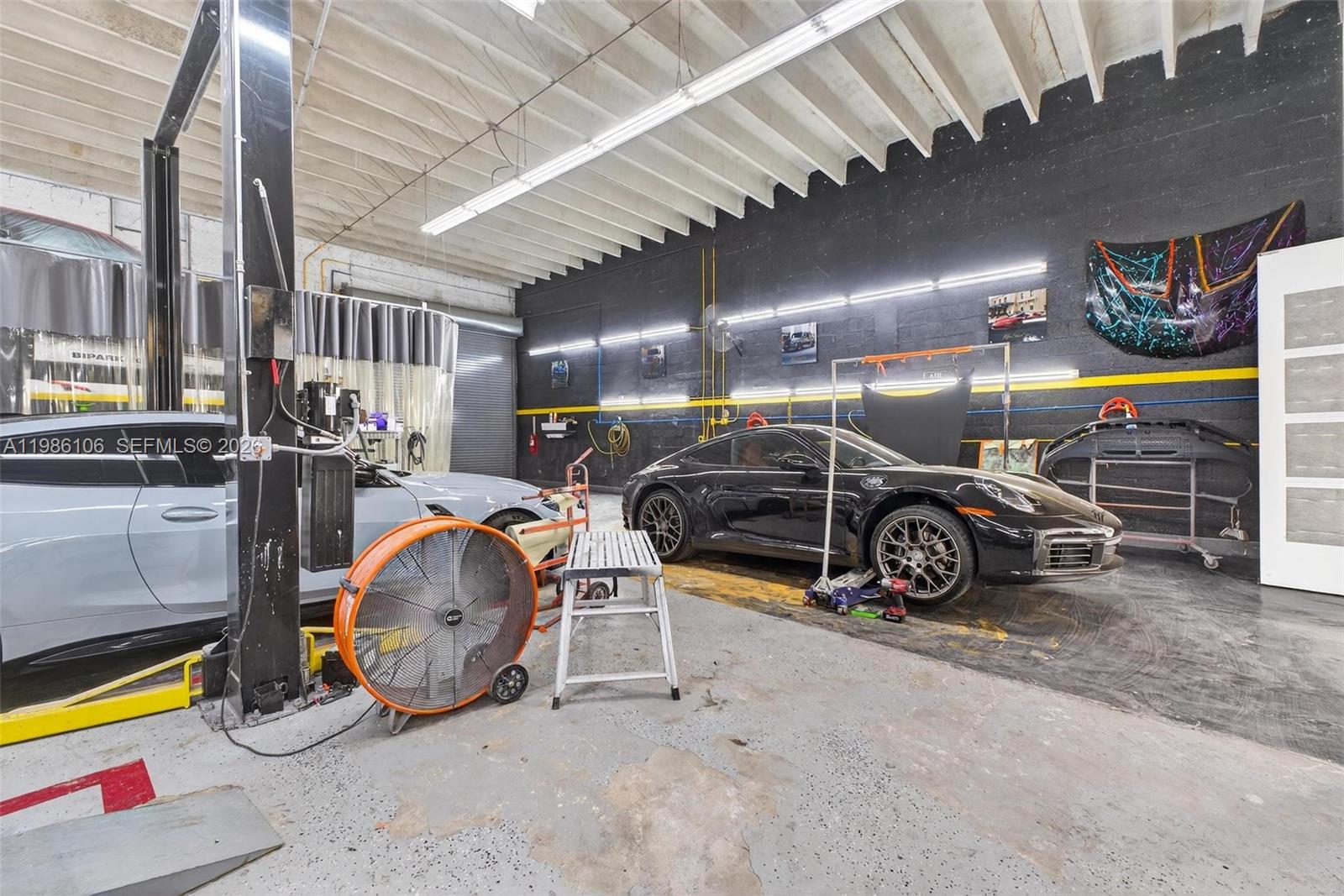 A garage workspace features two luxury sports cars, a vehicle lift, and industrial lighting — 0000 NW 56, Doral FL 33166, DORAL, FL