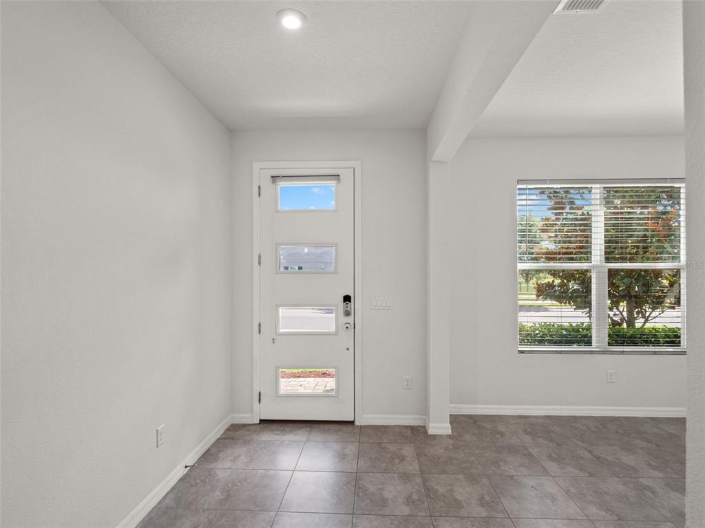 An entryway features a white front door with four glass panels and gray tile flooring — 9008 EXPLORATION AVENUE, ORLANDO, FL