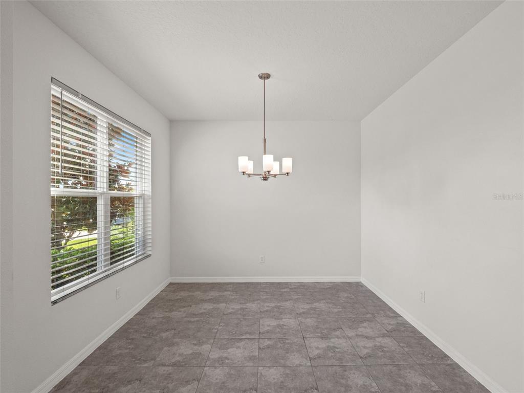 A dining area with gray tile flooring, white walls, and a hanging chandelier — 9008 EXPLORATION AVENUE, ORLANDO, FL