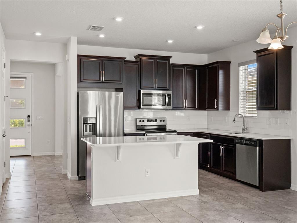 A kitchen with dark wood cabinets, stainless steel appliances, a white island, and tile flooring — 9008 EXPLORATION AVENUE, ORLANDO, FL