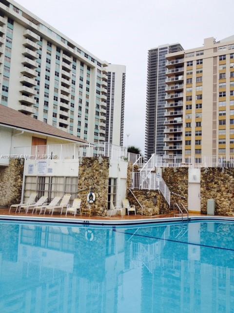 A swimming pool sits in front of a stone-walled patio and two tall apartment buildings — 1833 S Ocean Dr # 308, Hallandale Beach FL 33009, HALLANDALE BEACH, FL