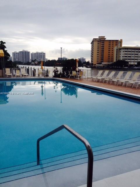 A swimming pool with a metal handrail overlooks a waterfront area with lounge chairs — 1833 S Ocean Dr # 308, Hallandale Beach FL 33009, HALLANDALE BEACH, FL