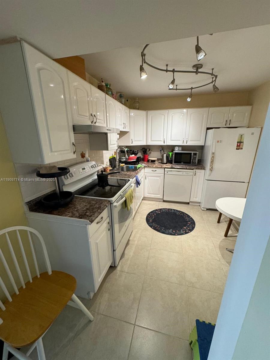 A kitchen features white cabinets, a dark countertop, stainless steel appliances, and tile flooring — 1833 S Ocean Dr # 308, Hallandale Beach FL 33009, HALLANDALE BEACH, FL