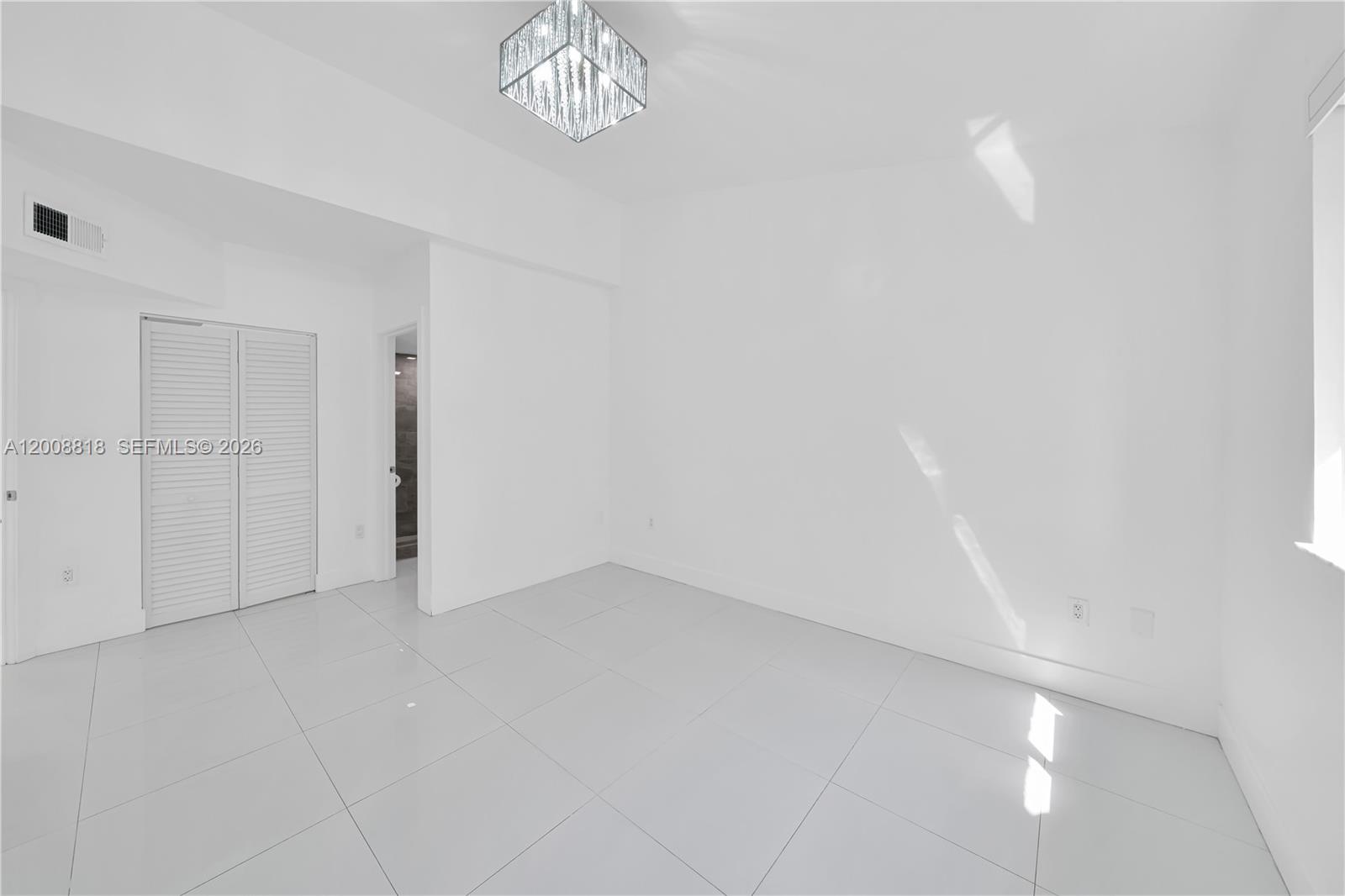 A bright, empty room features white walls, large light-colored floor tiles, and a modern chandelier — 13170 SW 66 Ter # 1810B, Miami FL 33183, MIAMI, FL