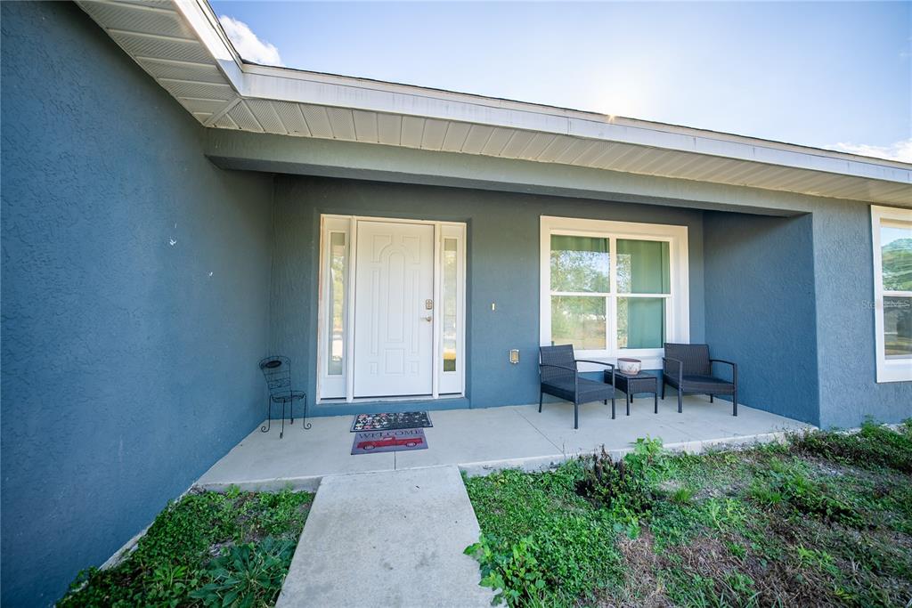 A blue house exterior features a covered front porch with a white door and chairs — 16417 SW 27TH CIRCLE, OCALA, FL