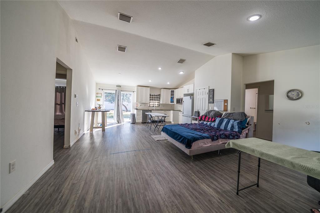 A large, open-concept living area features a kitchen, a bed, and light wood-look flooring — 16417 SW 27TH CIRCLE, OCALA, FL
