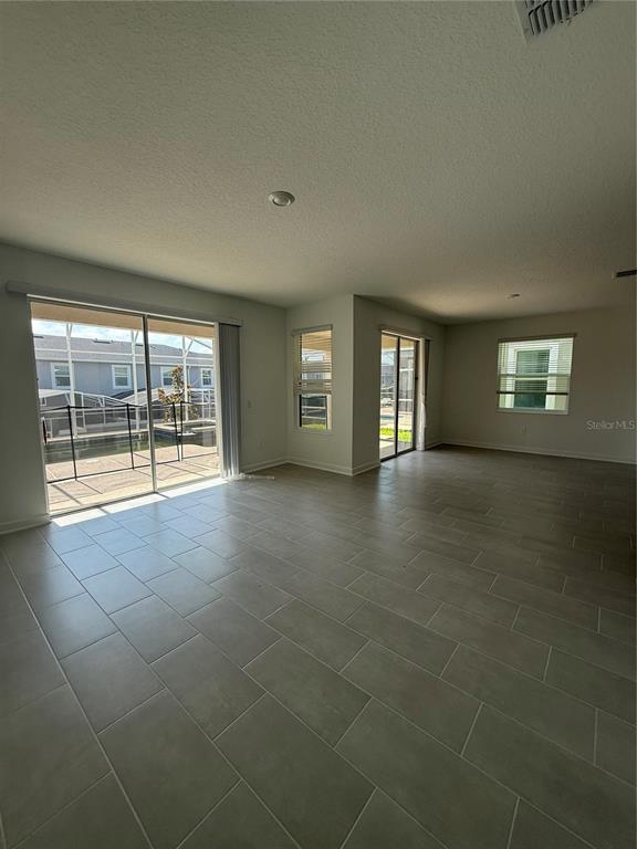 An open-concept living area features large tile flooring, sliding glass doors, and multiple windows — 1123 KINGSBARN STREET, DAVENPORT, FL