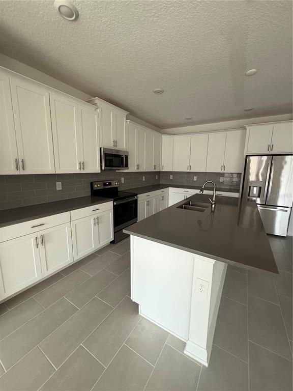 A modern kitchen features white cabinets, gray countertops, stainless steel appliances, and tile flooring — 1123 KINGSBARN STREET, DAVENPORT, FL