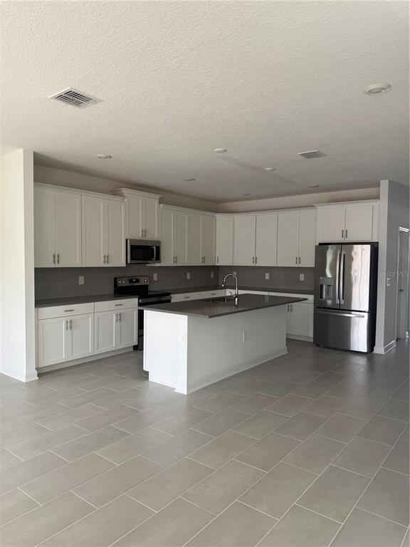 A kitchen features white cabinetry, stainless steel appliances, a center island, and gray tile flooring — 1123 KINGSBARN STREET, DAVENPORT, FL
