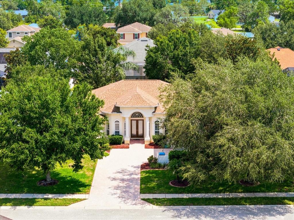 An aerial view of a single-story house with a paved driveway and mature trees — 13519 BARKINGSIDE PLACE, SPRING HILL, FL