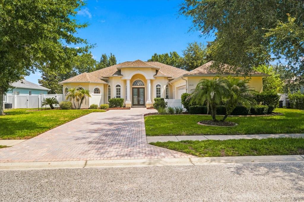 A single-story house with a beige stucco exterior, a brick driveway, and a covered entryway — 13519 BARKINGSIDE PLACE, SPRING HILL, FL
