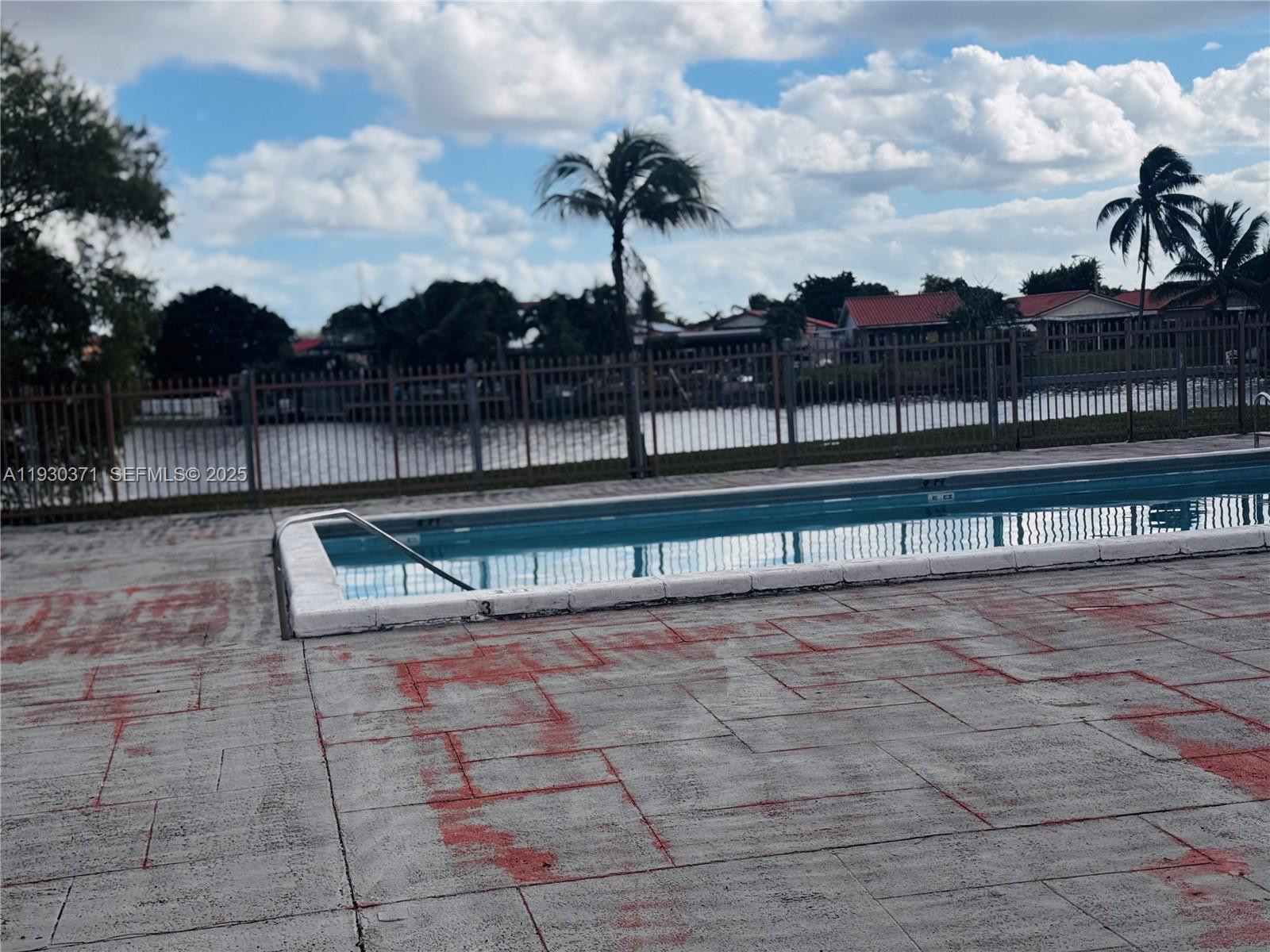 A swimming pool with a metal fence overlooks a canal under a cloudy sky — 6455 W 27th Ave # 13, Hialeah FL 33016, HIALEAH, FL