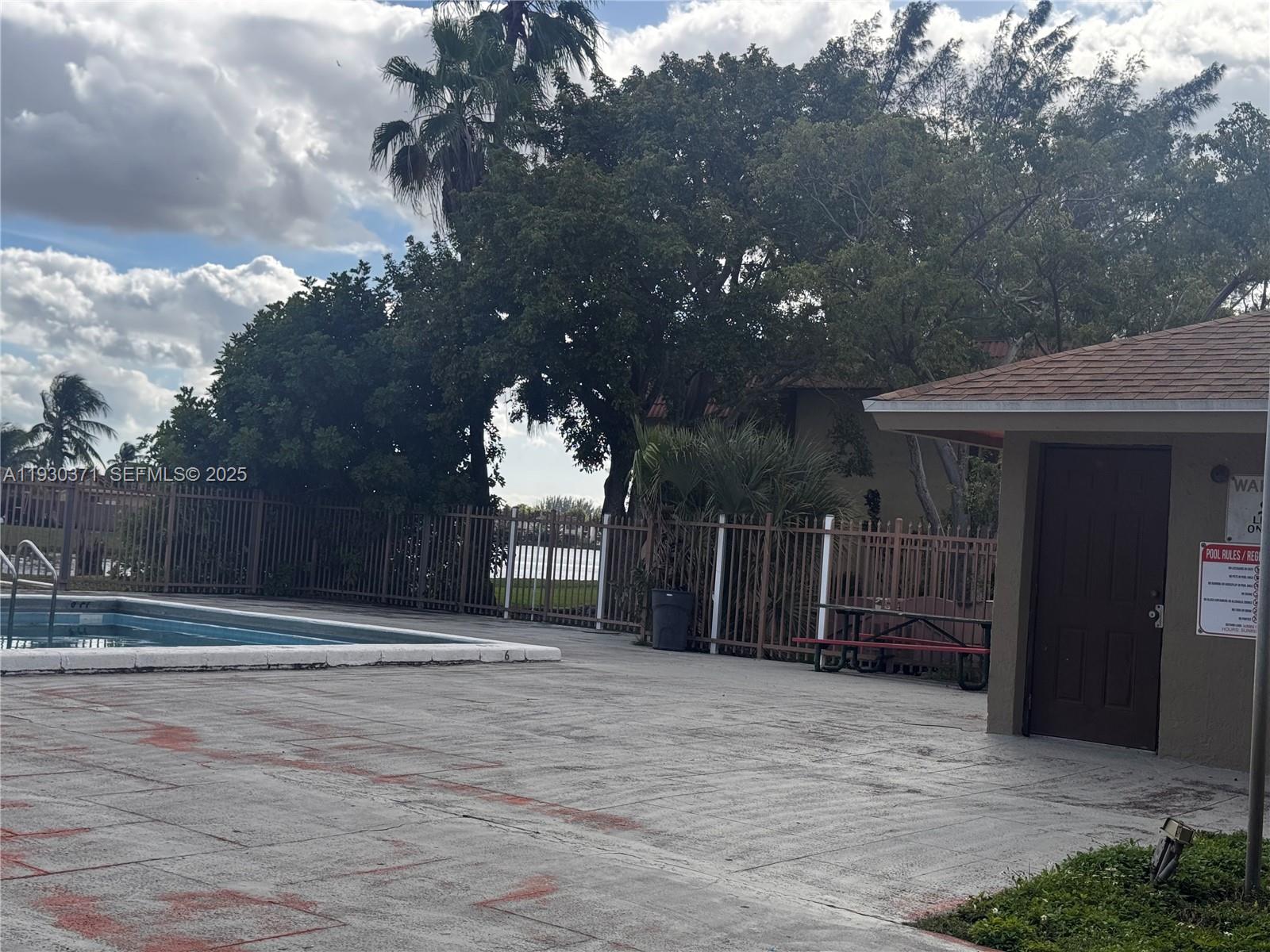 A swimming pool area features a concrete deck, a small building, and a metal fence — 6455 W 27th Ave # 13, Hialeah FL 33016, HIALEAH, FL