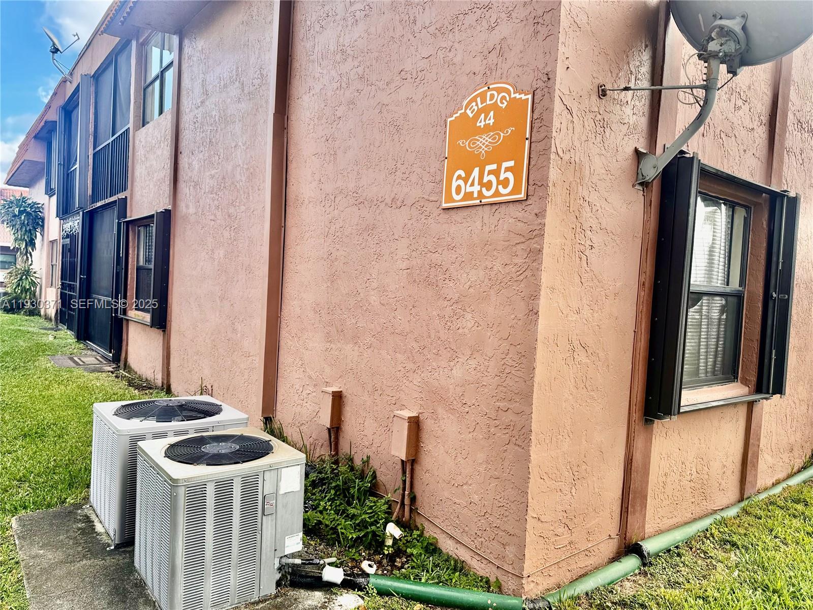 The exterior of a multi-story stucco building features two air conditioning units and a building sign — 6455 W 27th Ave # 13, Hialeah FL 33016, HIALEAH, FL