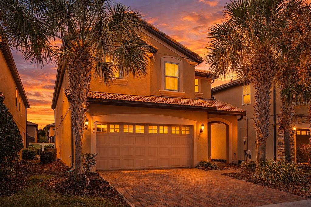 A two-story stucco house with a tiled roof, two-car garage, and palm trees at sunset — 2108 MOROCCO WAY, KISSIMMEE, FL
