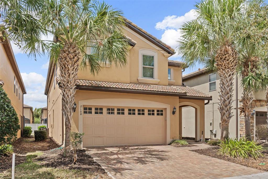 A two-story tan stucco house features a two-car garage, a tiled roof, and palm trees — 2108 MOROCCO WAY, KISSIMMEE, FL