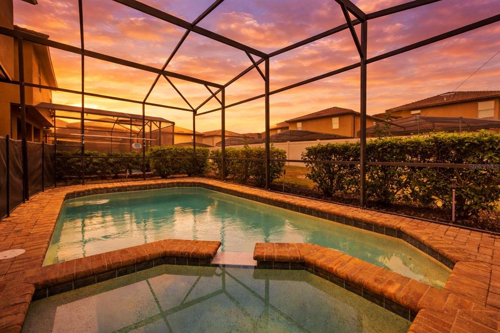 A screened-in swimming pool and spa area with brick coping at sunset — 2108 MOROCCO WAY, KISSIMMEE, FL