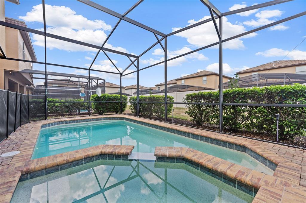 A screened-in swimming pool and spa with brick coping and surrounding hedges — 2108 MOROCCO WAY, KISSIMMEE, FL