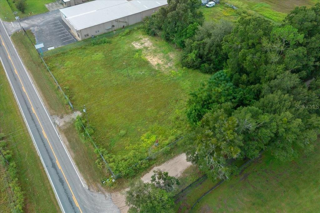 An aerial view shows a fenced, grassy vacant lot situated next to a commercial building — 16262 S HIGHWAY 475, SUMMERFIELD, FL