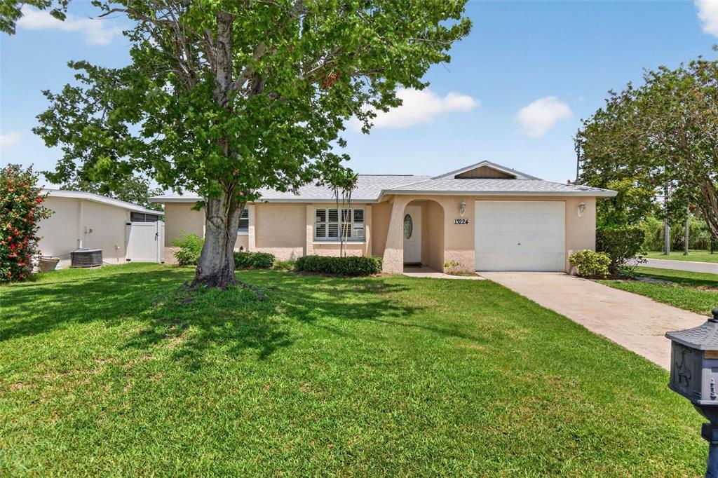 A single-story house with a beige stucco exterior, a white garage door, and a large tree — 13224 NEPTUNE DRIVE, HUDSON, FL