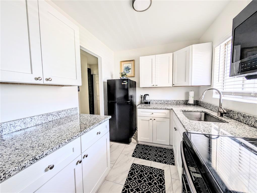 A kitchen features white cabinets, granite countertops, a black refrigerator, and black-and-white patterned floor mats — 1509 PLEASANT ROAD UNIT A4, BRADENTON, FL