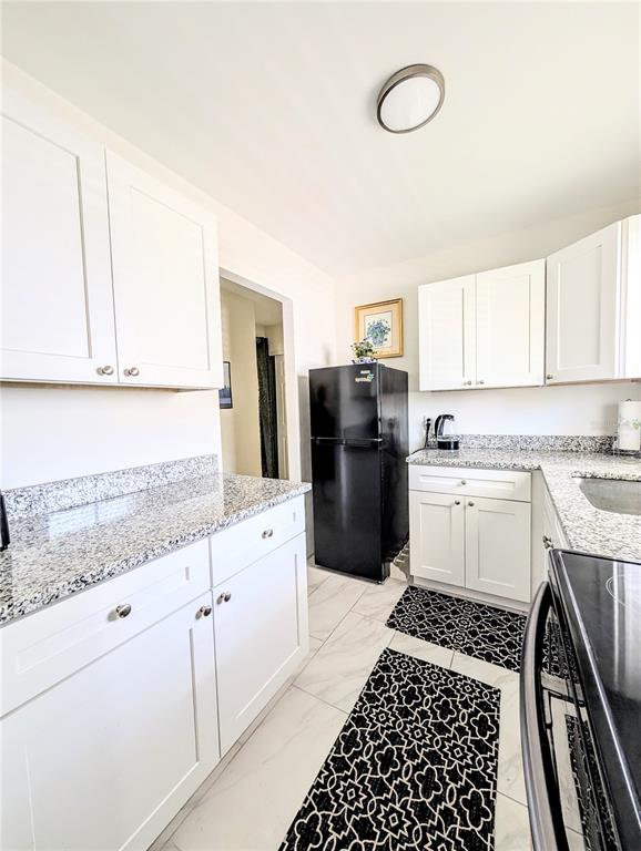 A kitchen features white cabinets, granite countertops, a black refrigerator, and patterned floor mats — 1509 PLEASANT ROAD UNIT A4, BRADENTON, FL