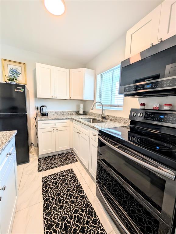 A kitchen features white cabinets, black appliances, granite countertops, and patterned rugs on tile floors — 1509 PLEASANT ROAD UNIT A4, BRADENTON, FL