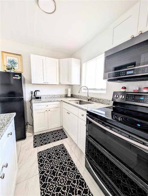 A kitchen features white cabinets, black appliances, and patterned rugs on a light-colored floor — 1509 PLEASANT ROAD UNIT A4, BRADENTON, FL