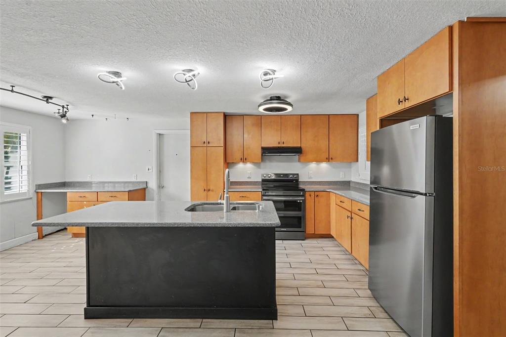 A kitchen features light wood cabinets, granite countertops, stainless steel appliances, and light-colored tile flooring — 986 LEXINGTON DRIVE, DUNEDIN, FL