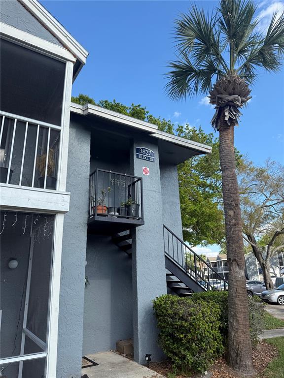A two-story gray apartment building exterior features a metal staircase and a palm tree — 3827 BAY CLUB CIRCLE UNIT 103, KISSIMMEE, FL