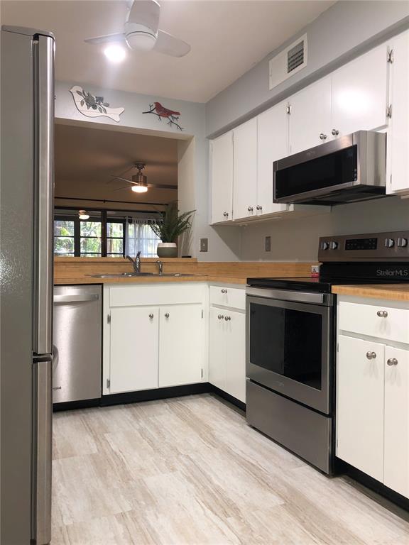 A kitchen with white cabinets, stainless steel appliances, and light wood-look flooring — 3399 MERMOOR DRIVE UNIT 206, PALM HARBOR, FL