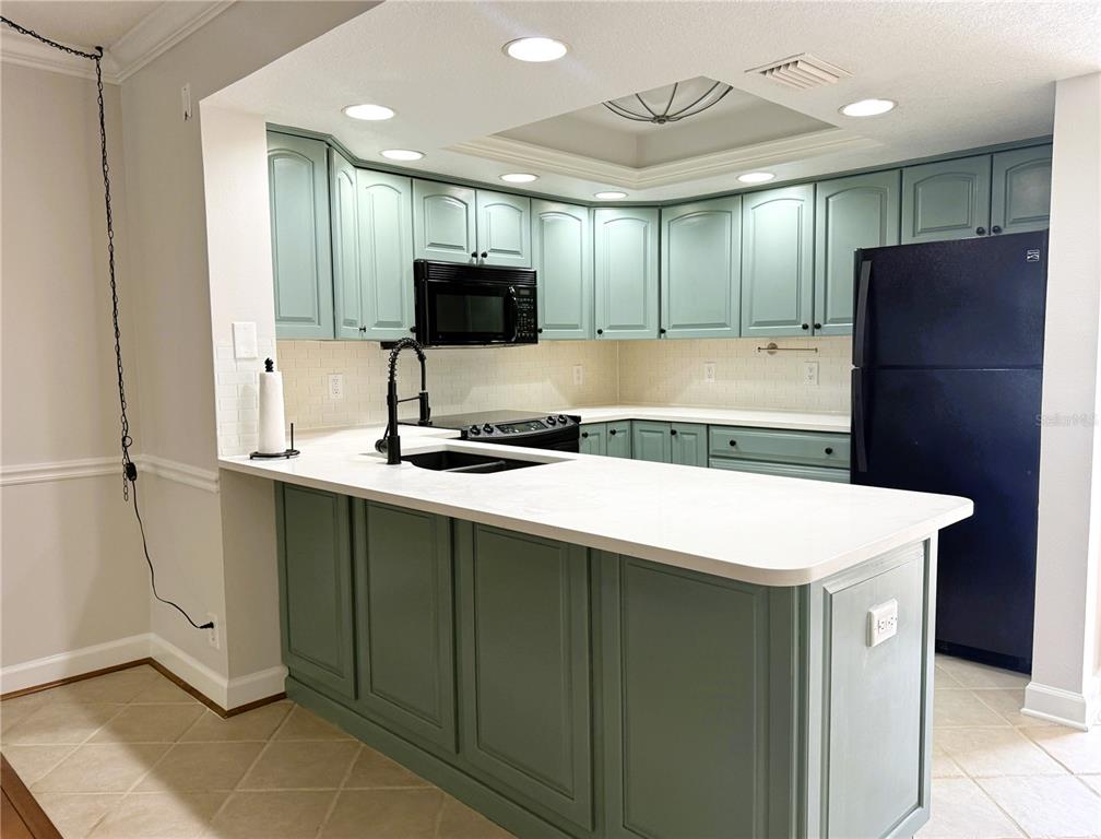 A kitchen features light blue cabinets, white countertops, a black refrigerator, and a breakfast bar — 2614 COVE CAY DRIVE UNIT 204, CLEARWATER, FL