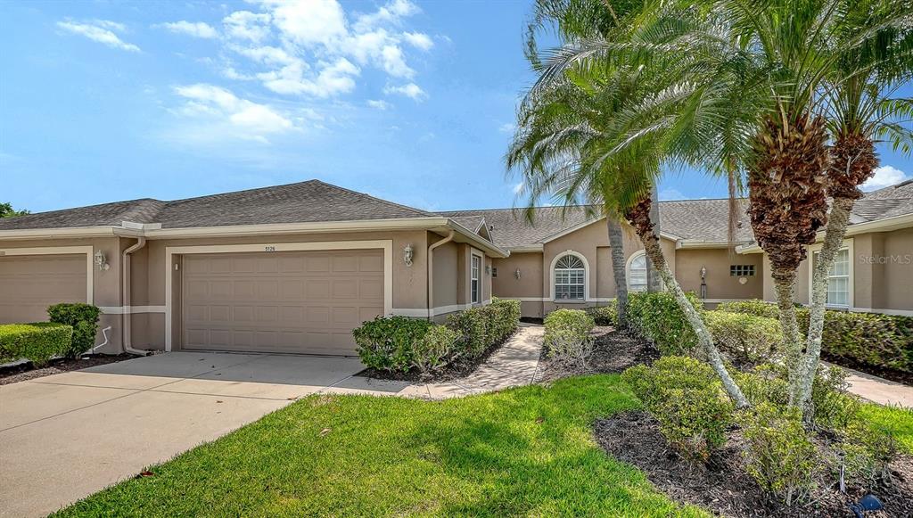 A beige house exterior features a two-car garage, a concrete driveway, and palm trees — 5126 BLUE ASH AVENUE, SARASOTA, FL